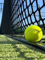 Yellow lonely ball by the net on the green padel court close up 