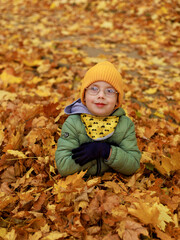 Dziecko siedzi i bawi się złotymi liśćmi klonu w parku jesienią. Widok z g&oacute;ry. Radość, relaks, czas spędzony na świeżym powietrzu. aktywny tryb życia.