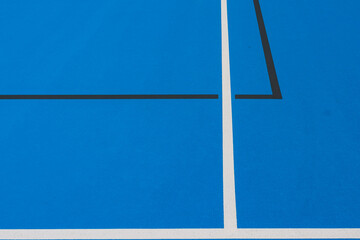 Close up photo of new outdoor blue tennis court with white lines combined with black pickleball lines.	