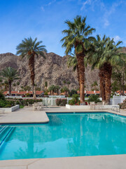 Outdoor swimming pool with seating areas amongst large palm trees near the mountains in Coachella Valley, California.