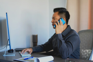 Busy young asian business man sales manager making phone call using laptop in office and talking on...