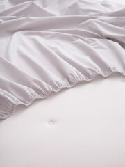 Close-up photo of the fitted sheet with an elastic band is laying on a white mattress. The sheet is rolled up. The part of the mattress surface is visible. Suitable for mockup