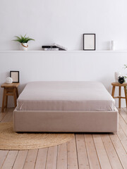 Minimalist interior bedroom with white walls, wooden floors, and double bed neatly covered with a grey sheet. The room is decorated with handcrafted furniture. Front view photo. Suitable for mockup