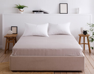 Modern bedroom with a minimalist interior, white walls, wooden floors and handcrafted furniture. Double bed with two pillows neatly covered with a fitted sheet. Front view photo. Suitable for mockup