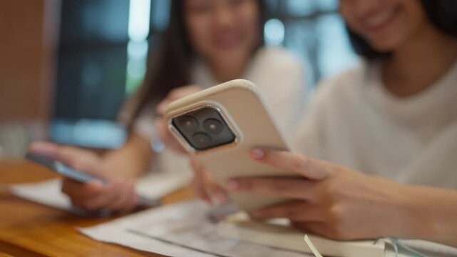 Two women are sitting at a table, each holding a cell phone. One of the women is looking at her phone while the other woman looks on. Concept of social interaction and communication