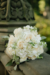 Elegant white floral bouquet rests on a stone ledge in a lush garden during daylight hours