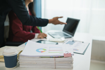 Two businesswomen are working together to search through important documents from a pile of documents on a table to verify the authenticity of the documents that were previously signed in a contract.