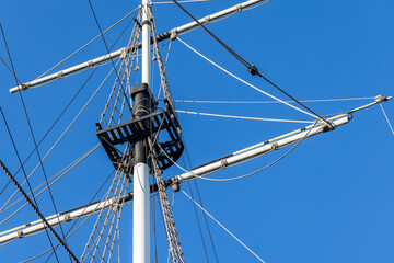 White ships mast, black platform, and rigged ropes are under blue sky