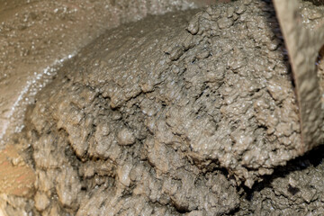 Wet gray mud with rough texture and small rocks. Macro shot of natural muddy surface.