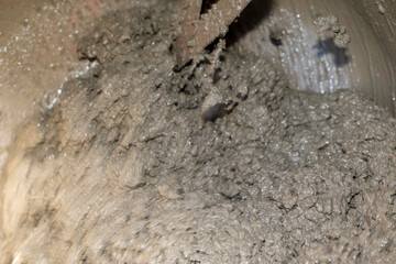 Wet gray mud with rough texture and small rocks. Macro shot of natural muddy surface.
