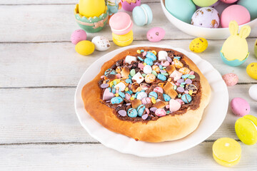 Sweet Easter dessert pizza, with chocolate paste topping, marshmallow and Easter chocolate eggs, snack for Easter holiday kids party, with festive decorations, colorful eggs and bunny rabbits