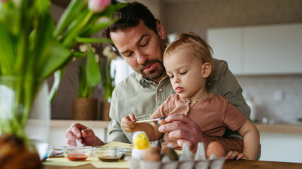 Father and little son decorating easter eggs at home.
