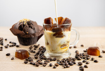 Side view of iced coffee drink, pouring milk in, coffee ice cubes scattered on table, decorated with coffee beans. Studio shot. Concept of coffee ice cubes for making strong drink.
