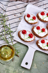 Creative tartines with white cheese and tomato cherries rest on a white board on a green table and a striped napkin