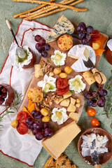 creative serving of cheese board with different cheeses, pistachio honey, fruits, nuts, white wine and floral decoration on green background