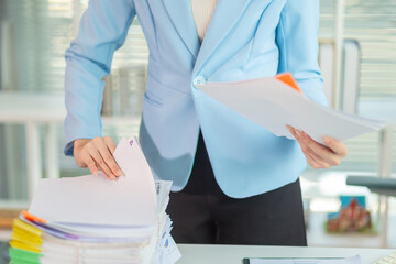 Businessman searching for important contract documents from pile of documents on table confirm agreement she signed with an investor. Businessman checking accuracy of documents she signed in contract