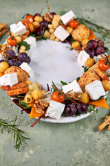 oval dish with a wreath of cheese and meat appetizers with vegetables on a green table, creative serving view from above