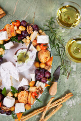 oval dish with a wreath of cheese and meat appetizers with vegetables on a green table, creative serving view from above