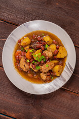 On the plate on the table is chelnt with potatoes, beans, onions, meat, spices and dates. Vertical photo.