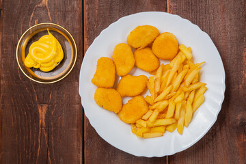 French fries and golden nuggets with cheese sauce on a wooden table
