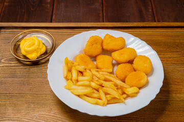 French fries and golden nuggets with cheese sauce on a small