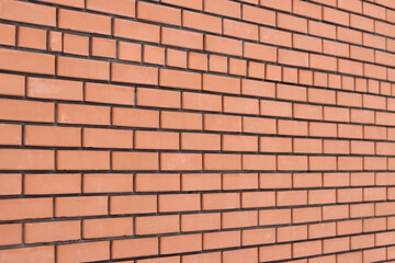 Fototapeta premium Brick wall background from the side with selective focus. Orange brick background for exterior design. Construction concept. Wall with classic checkerboard pattern and visible joints