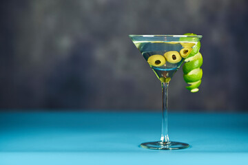Refreshing Martini glass with green olives inside, on a sky blue and grey surface