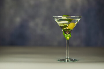 Refreshing Martini glass with green olives inside, on a grey surface