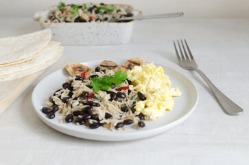 Costa Rican dish - Gallopinto. Black beans and rice with onions, garlic, cilantro in a ceramic plate with eggs and and grilled bananas on the table. Selective focus. Horizontal orientation.