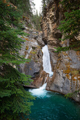 Powerful Johnston Canyon waterfall descending through rocky landscape, plunging into turquoise...
