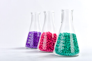 Red, purple and turquoise masterbatch granules in Erlenmeyer flask isolated on white background,...