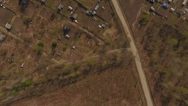 A top-down view of a countryside village with scattered houses, fenced plots, and unpaved roads surrounded by dry fields and sparse vegetation