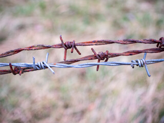 A close-up of two layers of barbed wire, one rusty and aged, the other newer and silver. The...