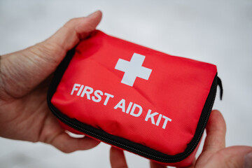 A person is firmly holding a bright red first aid kit tightly in their hands, ready to provide any...