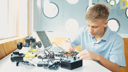 Caucasian boy fixing main board while study construction by using laptop analysis data. Young technician repairing and learning about using industrial structure at STEM technology class. Edification.