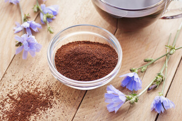 Ground chicory root powder in a bowl, healthy coffee substitude drink in a glass cup with flowers on rustic wooden background, closeup, natural medicine and naturopathy concept