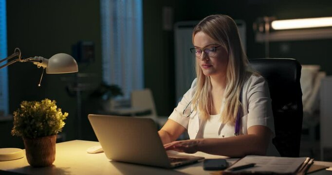 A dedicated medical worker focused on tasks at night, illuminated by warm light in a clinical setting.