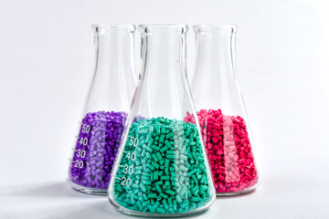 Red, purple and turquoise masterbatch granules in Erlenmeyer flask isolated on white background,...