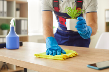 Close up of male cleaner wiping desk with household detergent supplies. Man janitor washing table at home or workplace in office. Cleaning service, housework and housekeeping concept