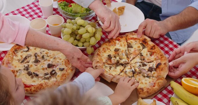 Family eating pizza. Group unrecognizable people having dinner enjoying two takeout or homemade pizzas. Cropped shot hands taking slices from board on red white gingham vichy check pattern table cloth