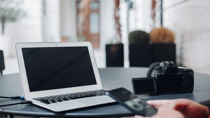 Photographer using laptop, smartphone and digital camera editing photos in bright workspace