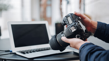 Photographer reviewing photos on professional digital camera after photoshoot, with laptop in background