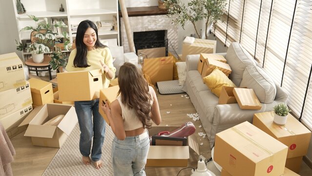 Top down view of asian couple holding cardboard box while dancing in to house at moving day. Attractive lesbian couple carrying package while moving in to new house and moving to music. Myrmidon. - Powered by Adobe