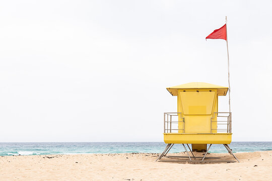 Bright yellow lifeguard tower on sandy beach with red flag