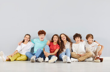 Group portrait of happy schoolchildren sitting together on a grey background. The students, friends, and pupils gather as a team, showcasing friendship, unity, and shared experiences in school life.