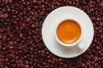 Cup of creamy coffee in white cup on coffee beans with copy space, top view.