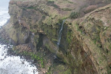 Obraz premium Coastal waterfall plunging into sea from cliffs between Scarborough and Whitby.