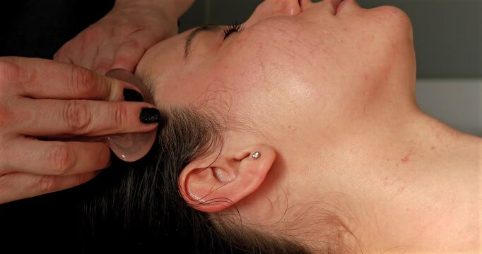 Young woman receiving facial massage with gua sha tool in beauty salon