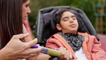 Mother feeding her son with cerebral palsy using a syringe