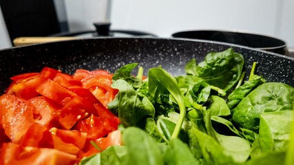 Close-up of fresh chopped tomatoes and vibrant spinach in a pan, ideal for healthy cooking, vegetarian diet, farm-to-table freshness